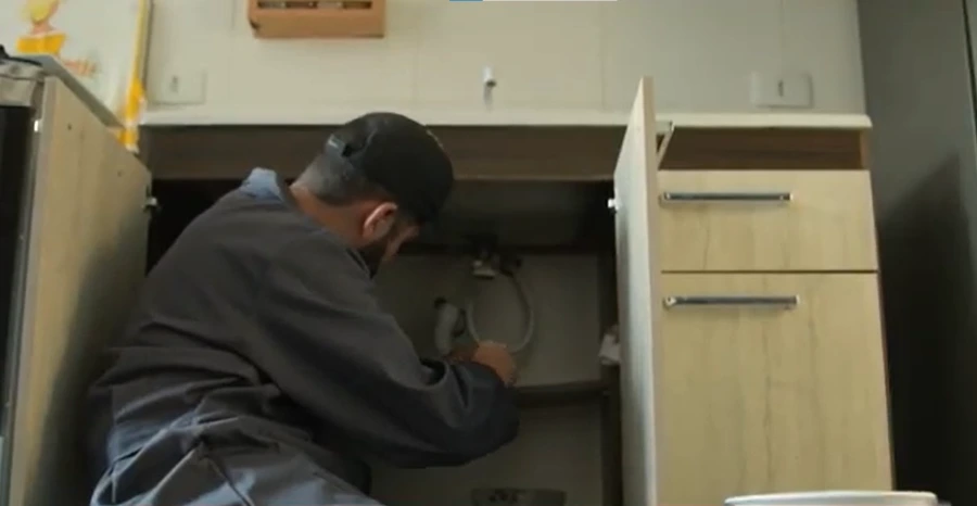 Plumber repairing pipe under kitchen sink in Pomona home